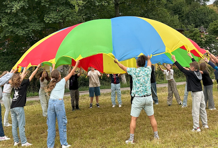 Bild: Das Bild zeigt Kinder in der Natur, die ein Regenbogen Schwungtuch nach oben steigen lassen.